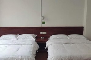 A hotel room with two single beds, a wooden headboard, a small bedside table, and a wall-mounted light switch. - Phoenix Hotel, Wuzhou (Wuzhou)