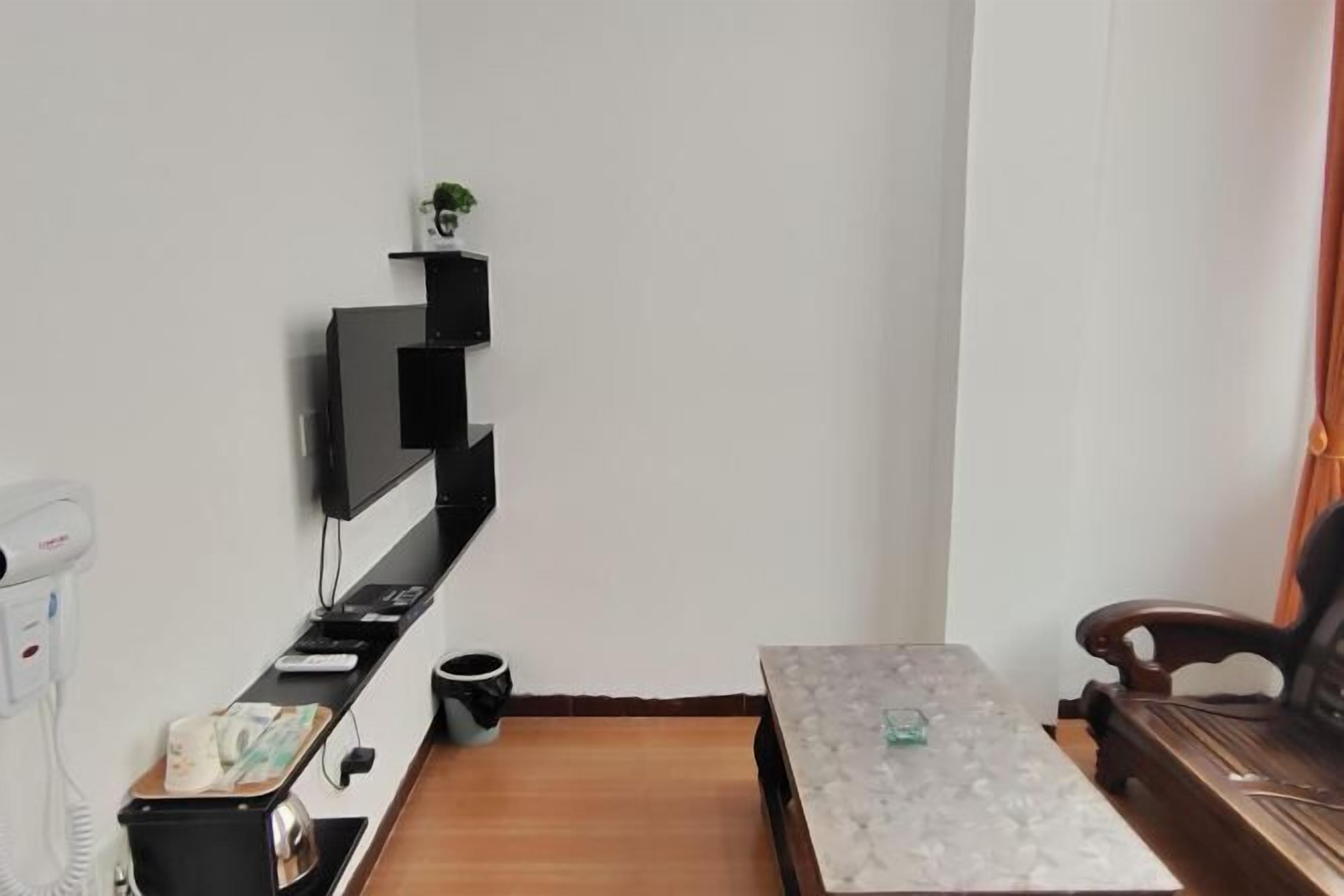A small, neatly organized room with a flat-screen TV mounted on the wall, a small table with a glass top, a wooden chair, and a trash bin.