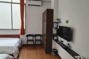 A hotel room with a bed, two chairs, a TV, a small shelf, and an air conditioning unit. - Phoenix Hotel, Wuzhou (Wuzhou)