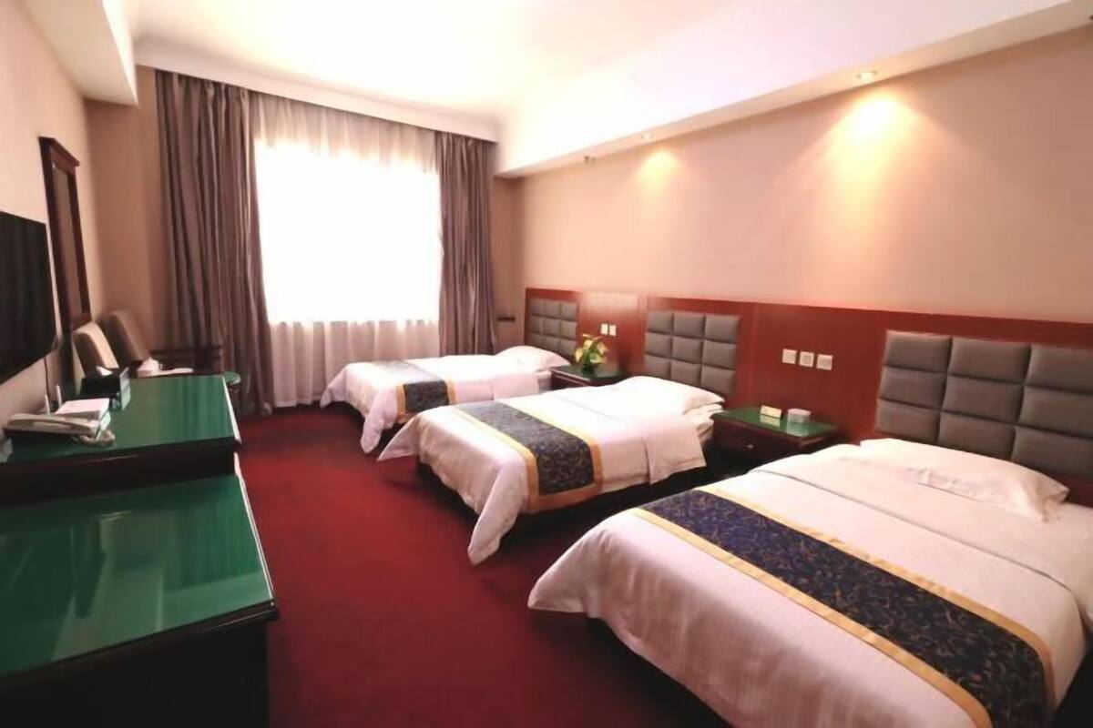 A hotel room with three beds, a desk, and a television.