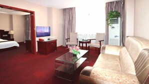 A hotel room with a bed, a sofa, a coffee table, a TV, a desk, and a window with curtains.