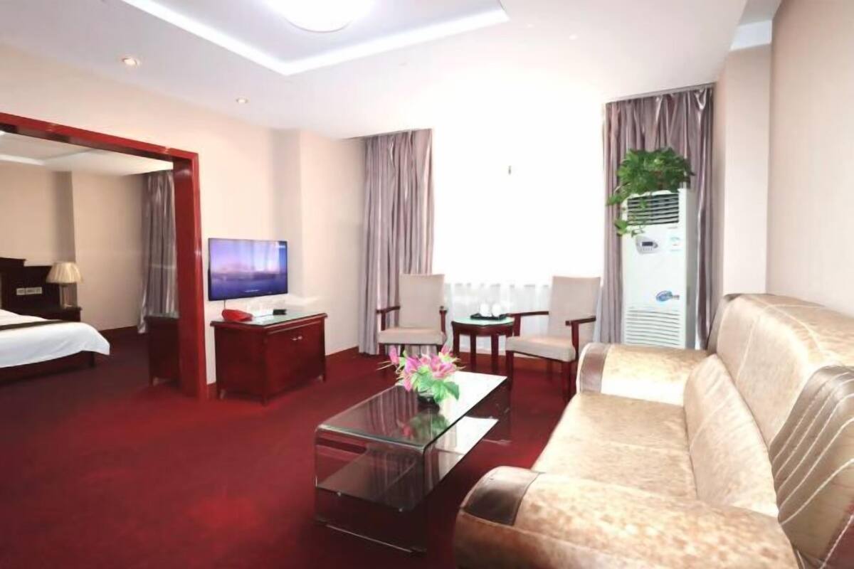 A hotel room with a bed, a sofa, a coffee table, a TV, a desk, and a window with curtains.