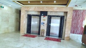 A lobby with marble flooring, two elevators, and a red patterned wall.