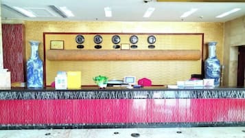 A reception desk with a red and black marble counter, a wooden panel with clocks, and two large vases on either side.