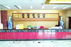 A reception desk with a red and black marble counter, a wooden panel with clocks, and two large vases on either side.