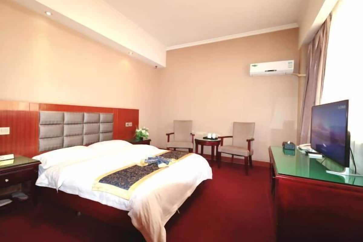 A hotel room with a bed, a desk, a chair, a TV, and an air conditioning unit.