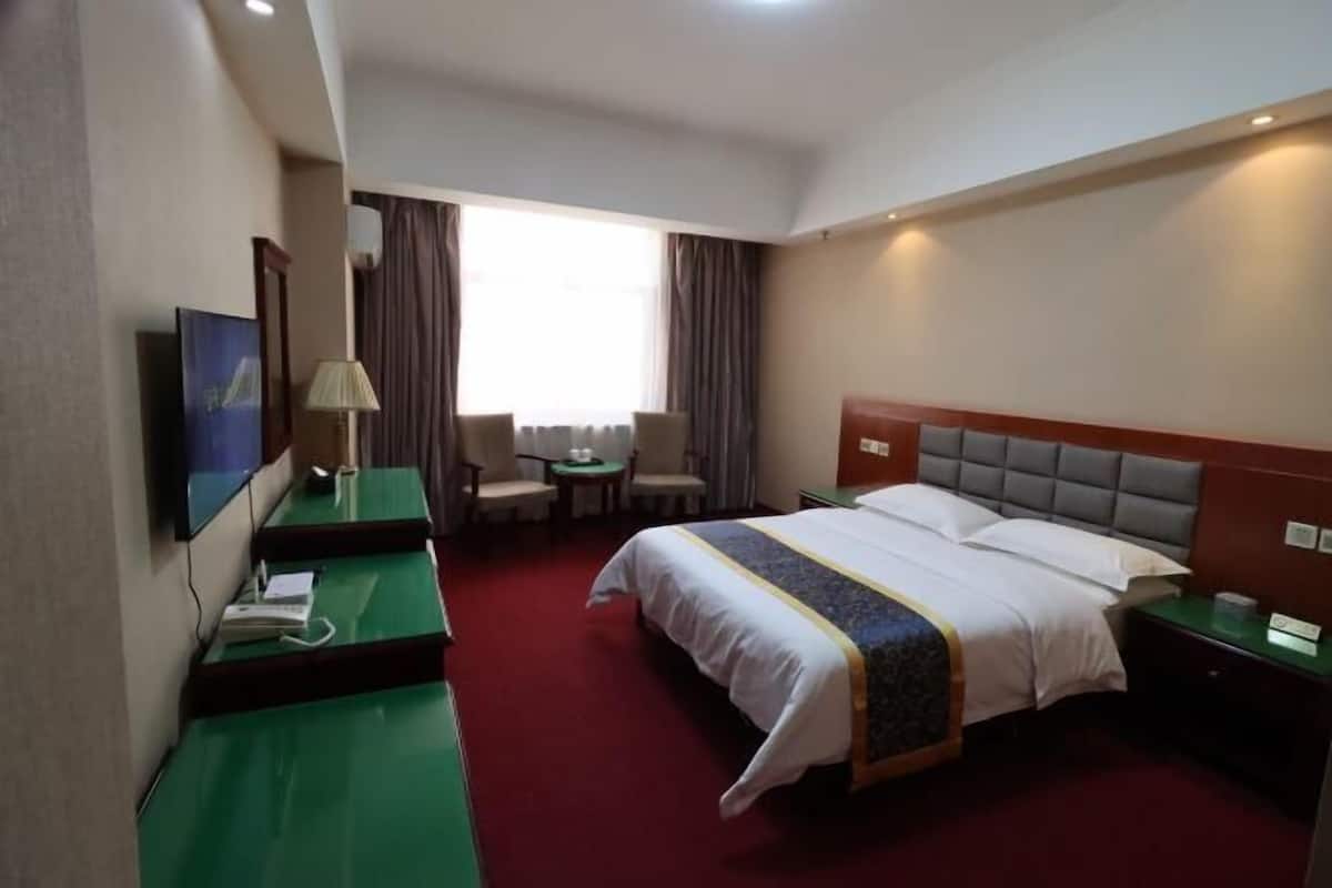 A hotel room with a bed, a desk, a chair, a TV, and a window with curtains.