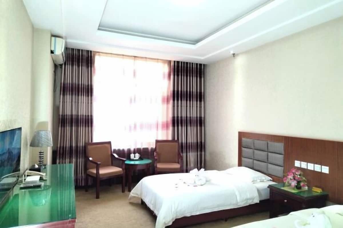 A hotel room with a bed, a desk with a lamp, two chairs, a small table, and a TV.
