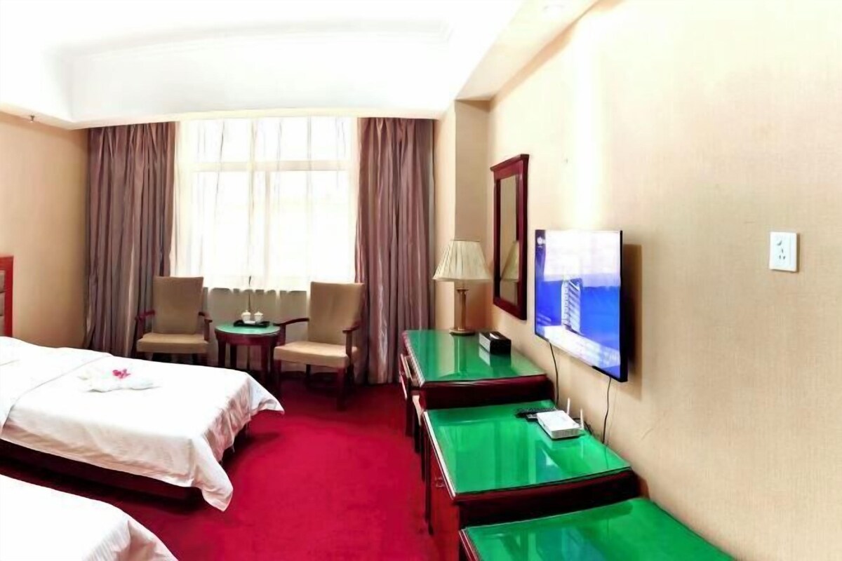 A hotel room with two beds, a TV, a desk, and a chair.