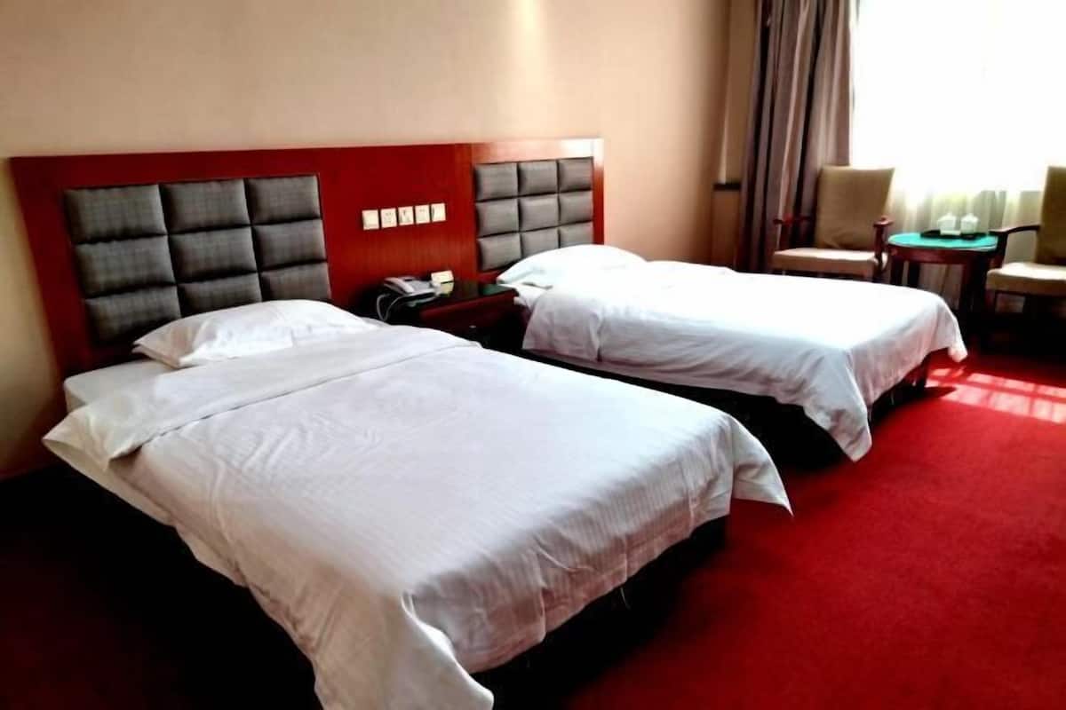 A hotel room with two beds, a red carpet, a wooden headboard, and a small table with chairs.