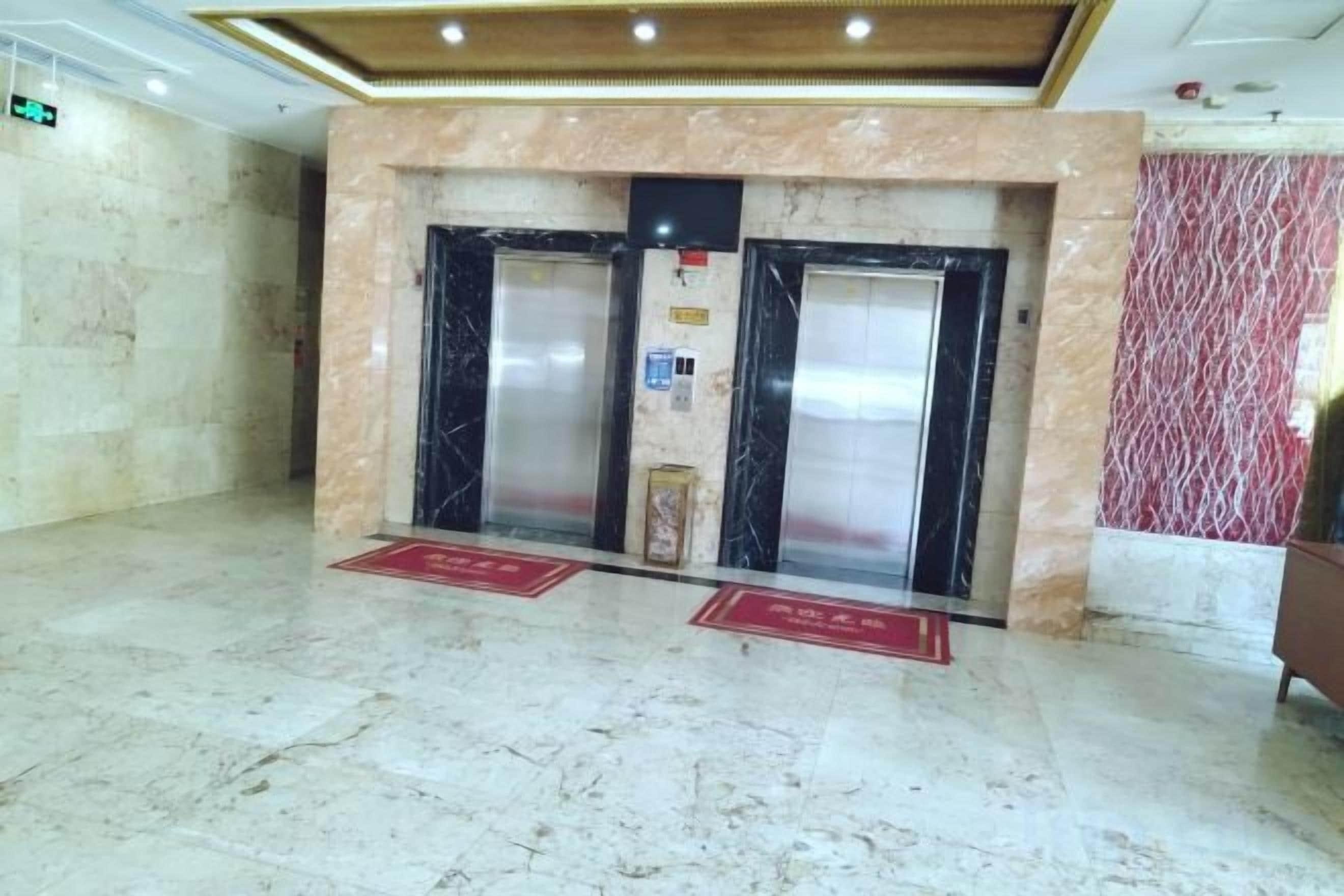 A lobby with marble flooring, two elevators, and red informational signs.