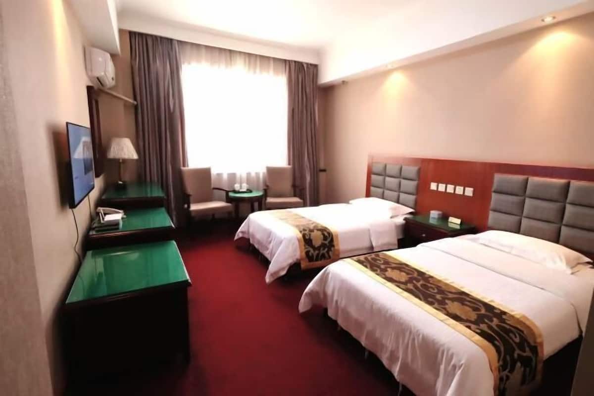 A hotel room with two beds, a desk, a chair, a TV, and a window with curtains.