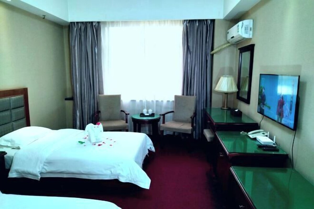 A hotel room with two beds, a desk, a chair, a TV, and a window with curtains.