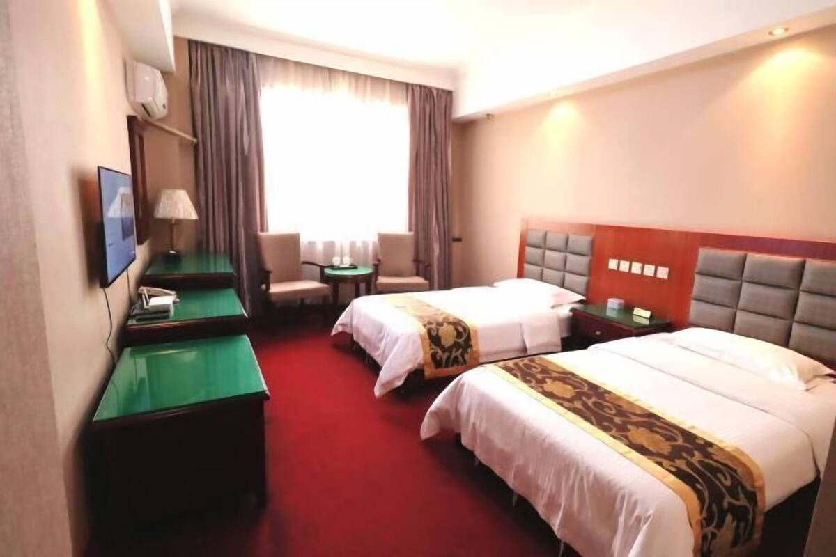 A hotel room with two beds, a desk, a chair, a TV, and a window with curtains.