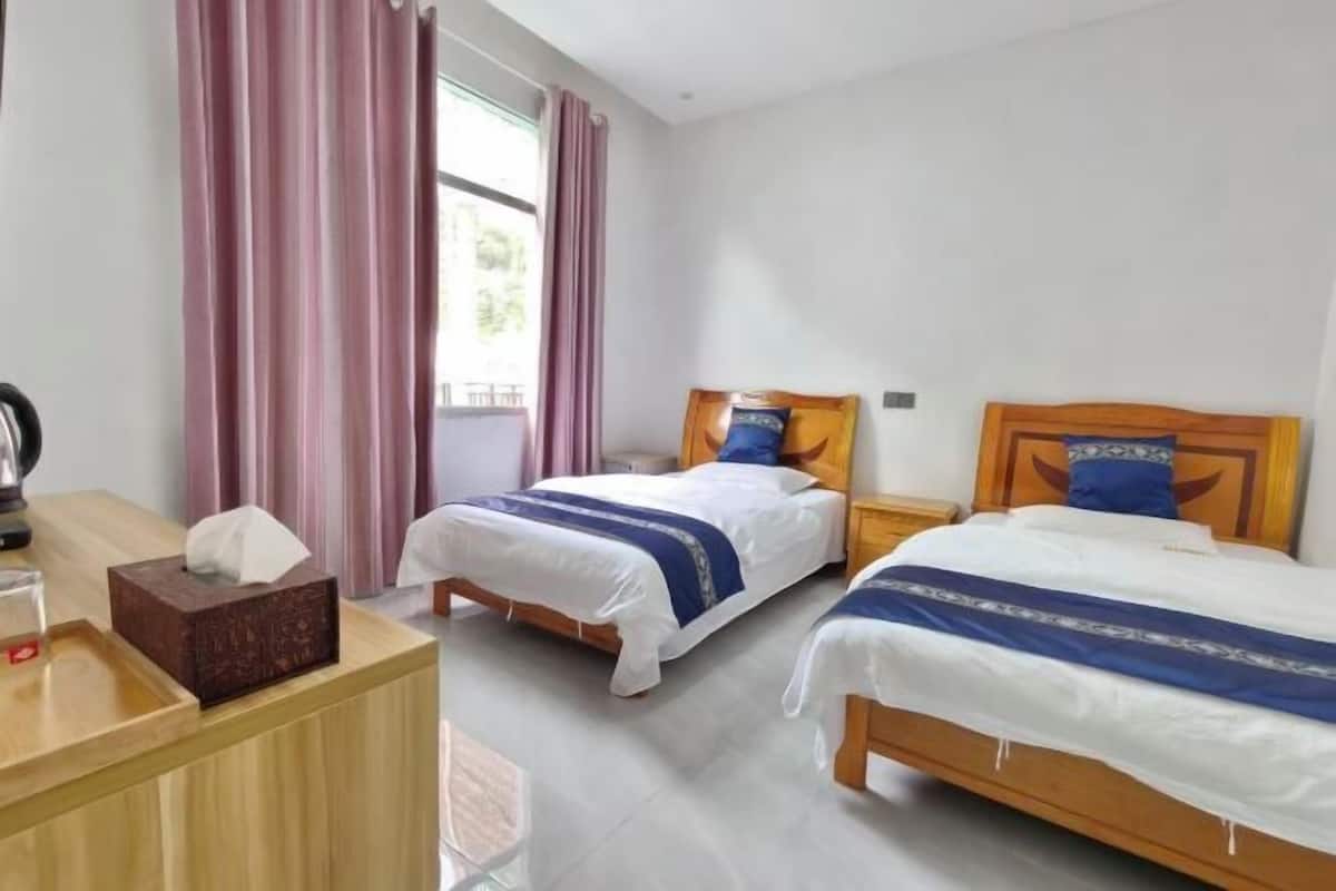 Habitación de hotel con dos camas, un escritorio de madera, una mesita de noche y una ventana con cortinas.