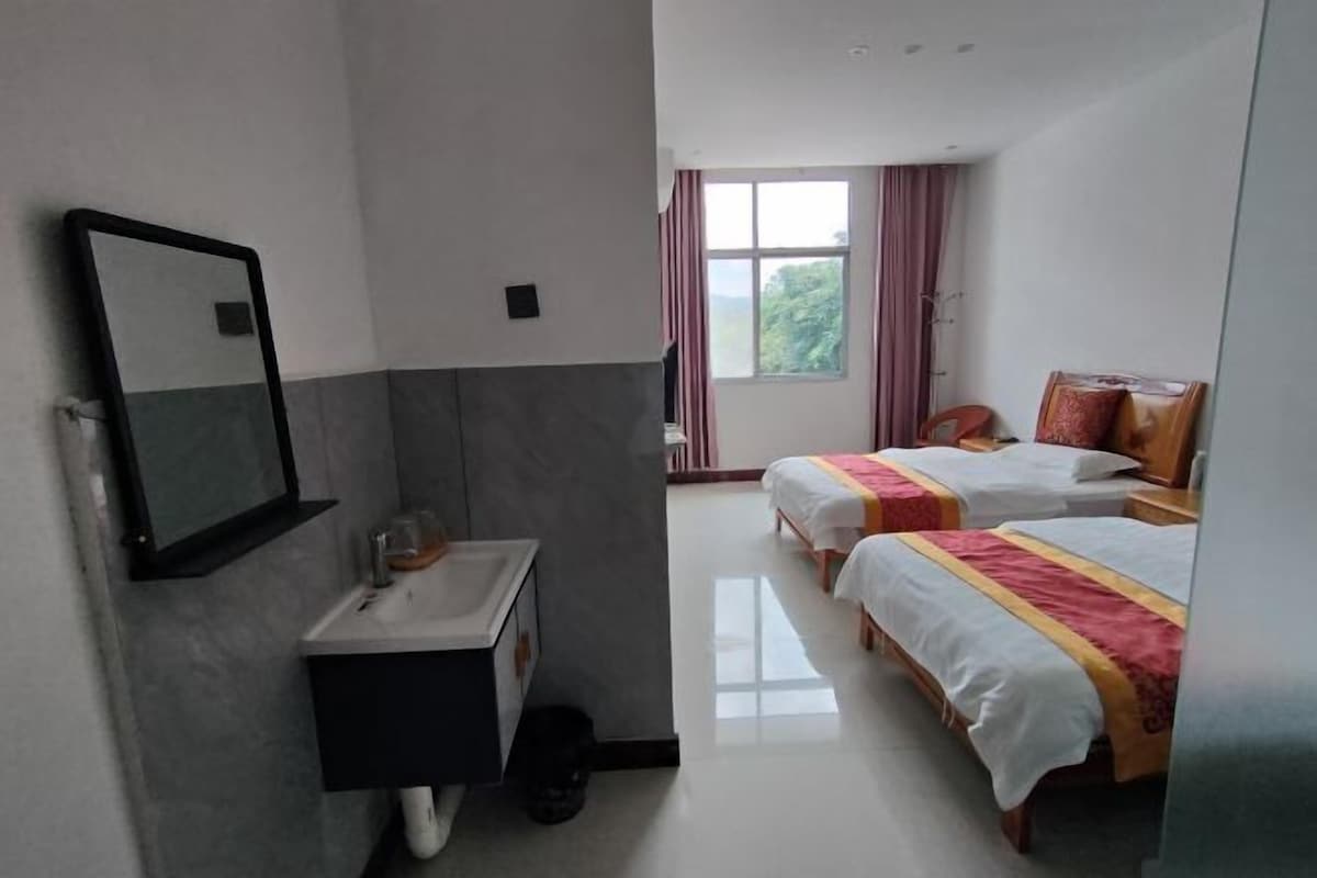 A hotel room with a bathroom, two beds, a window with curtains, and a mirror.