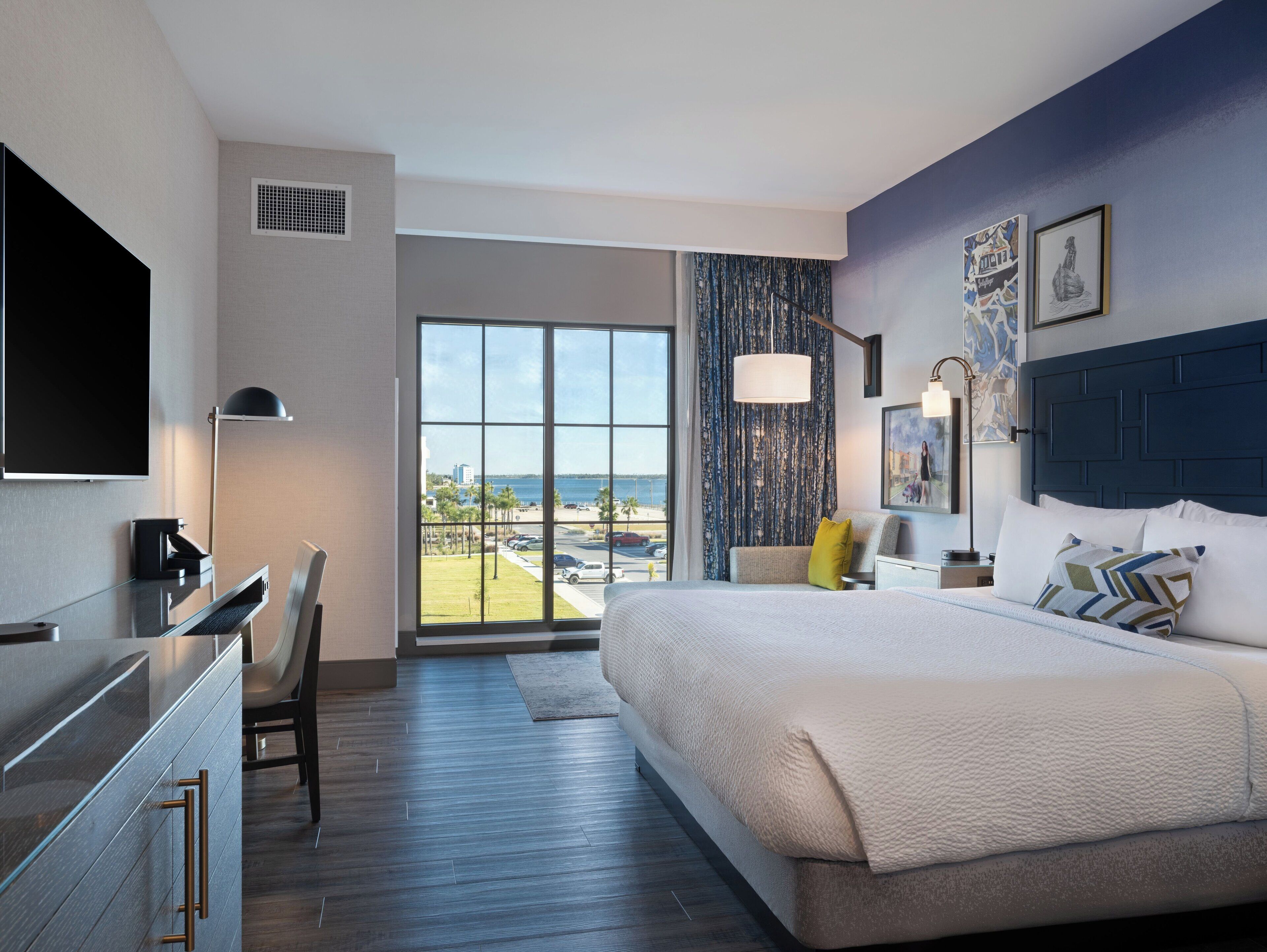 Habitación de hotel moderna con una cama grande, un escritorio, una silla, un televisor de pantalla plana y vistas a la playa.