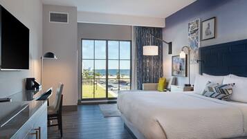 Habitación de hotel moderna con una cama grande, un escritorio, una silla, un televisor de pantalla plana y vistas a la playa.