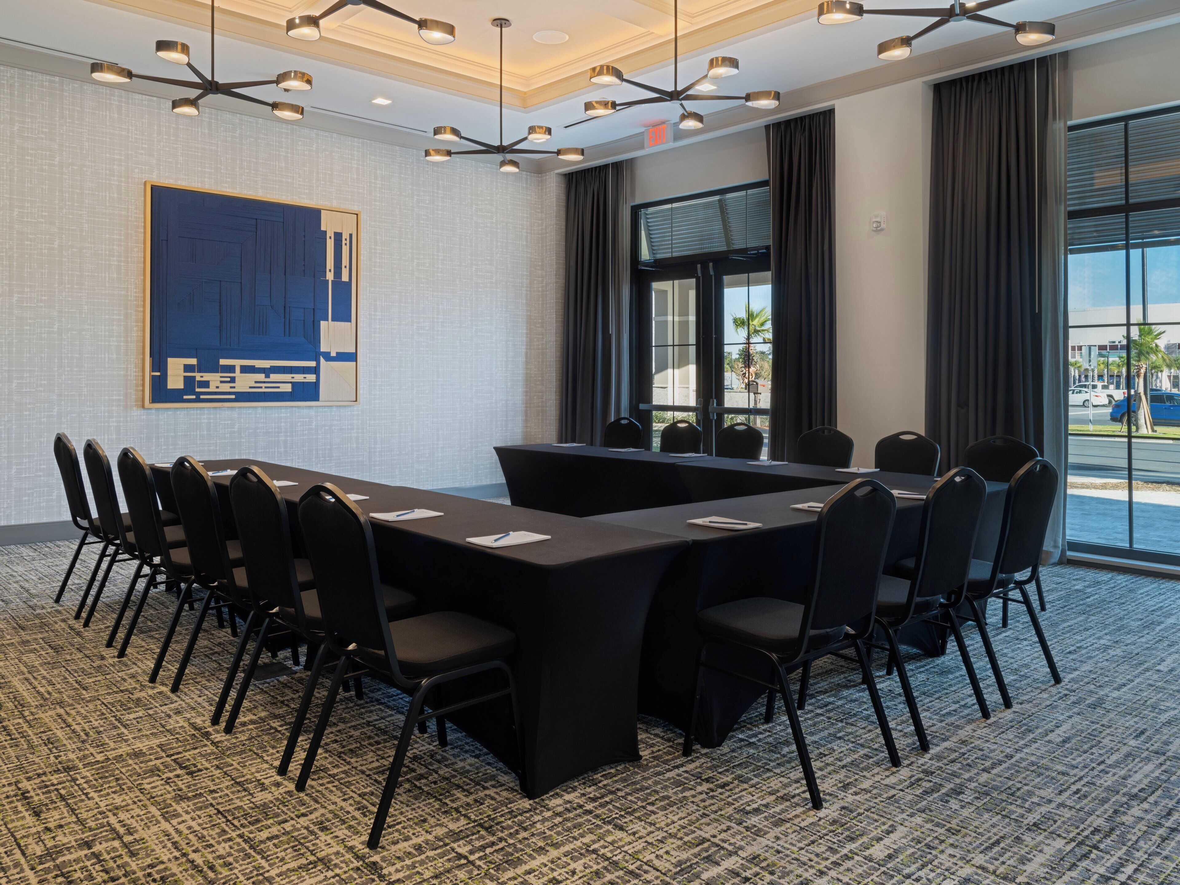 A conference room with a long table, chairs, a large abstract painting, and a view of the outside.