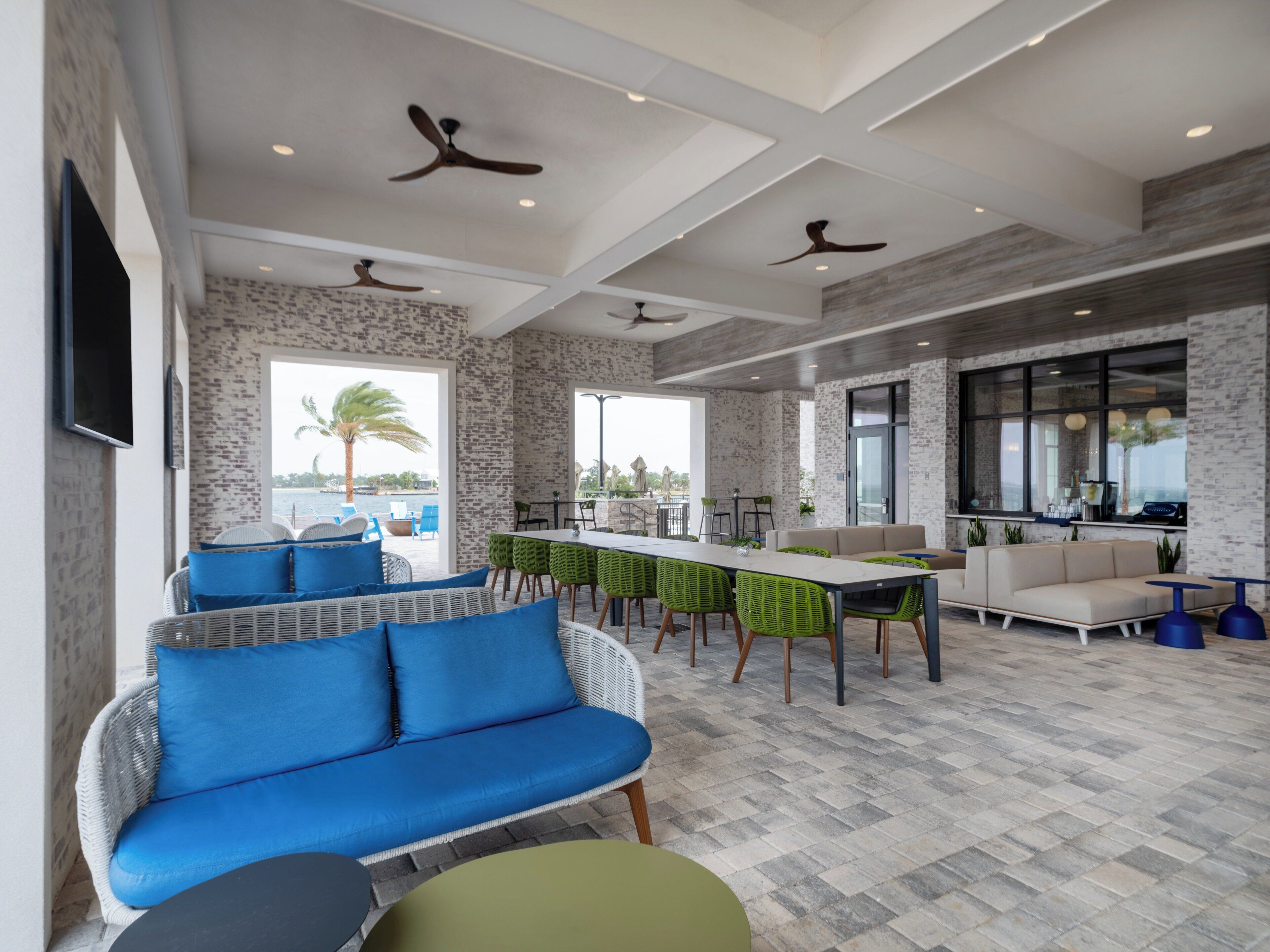 A spacious indoor area with a long dining table, multiple chairs, a sofa, and ceiling fans.