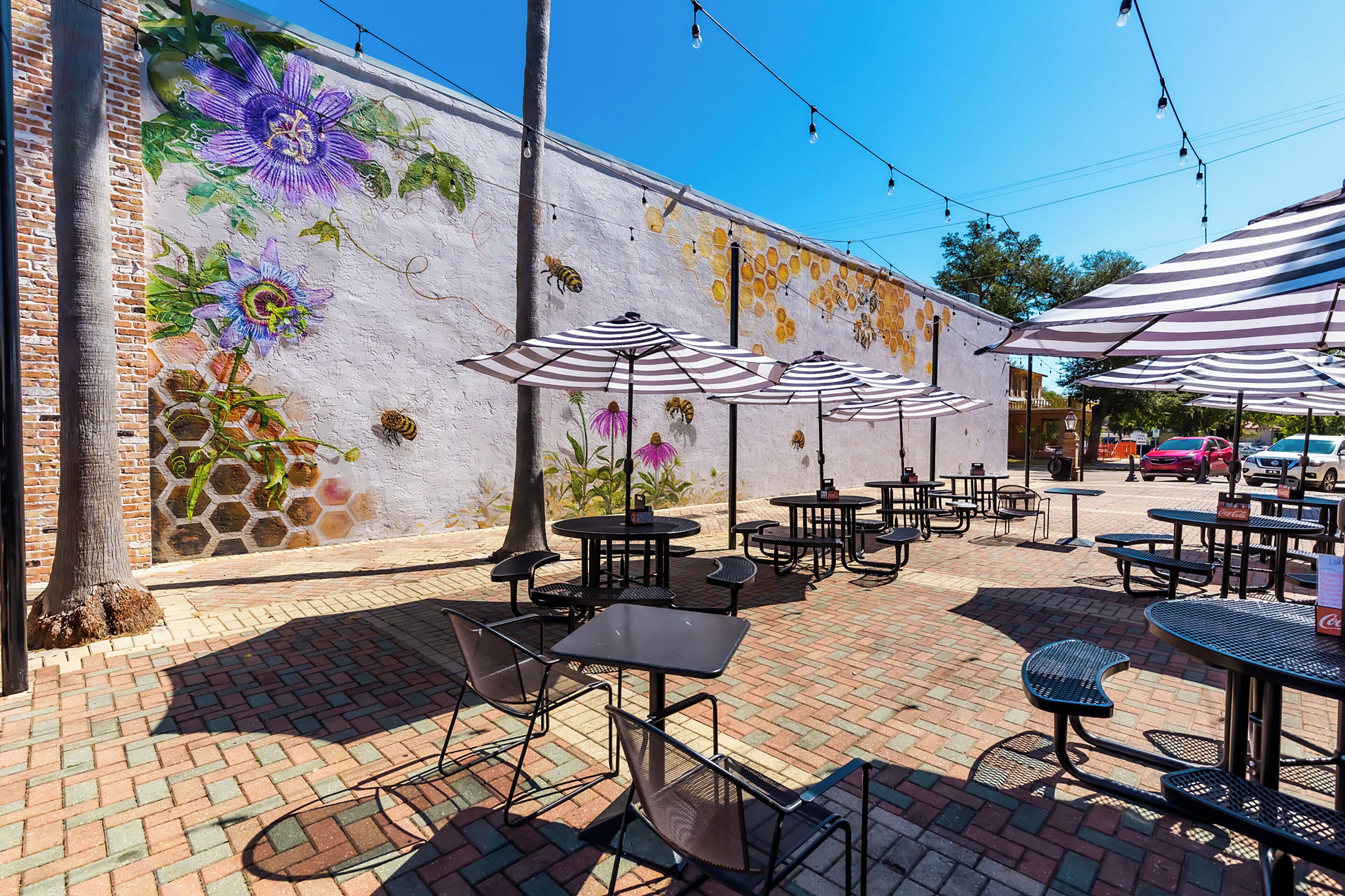 Un patio al aire libre con mesas y sillas, un mural en la pared y guirnaldas de luces.