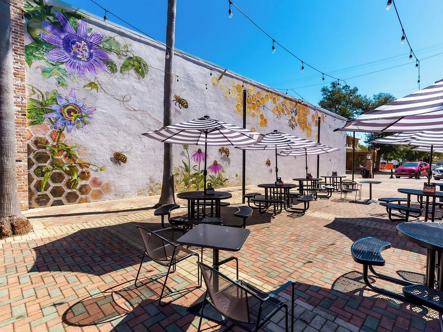 Un'area patio all'aperto con tavoli e sedie, un murale sulla parete e luci decorative.