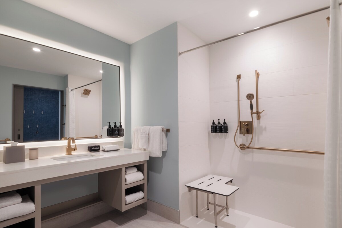 A modern bathroom with a large mirror, white vanity, and a shower area.