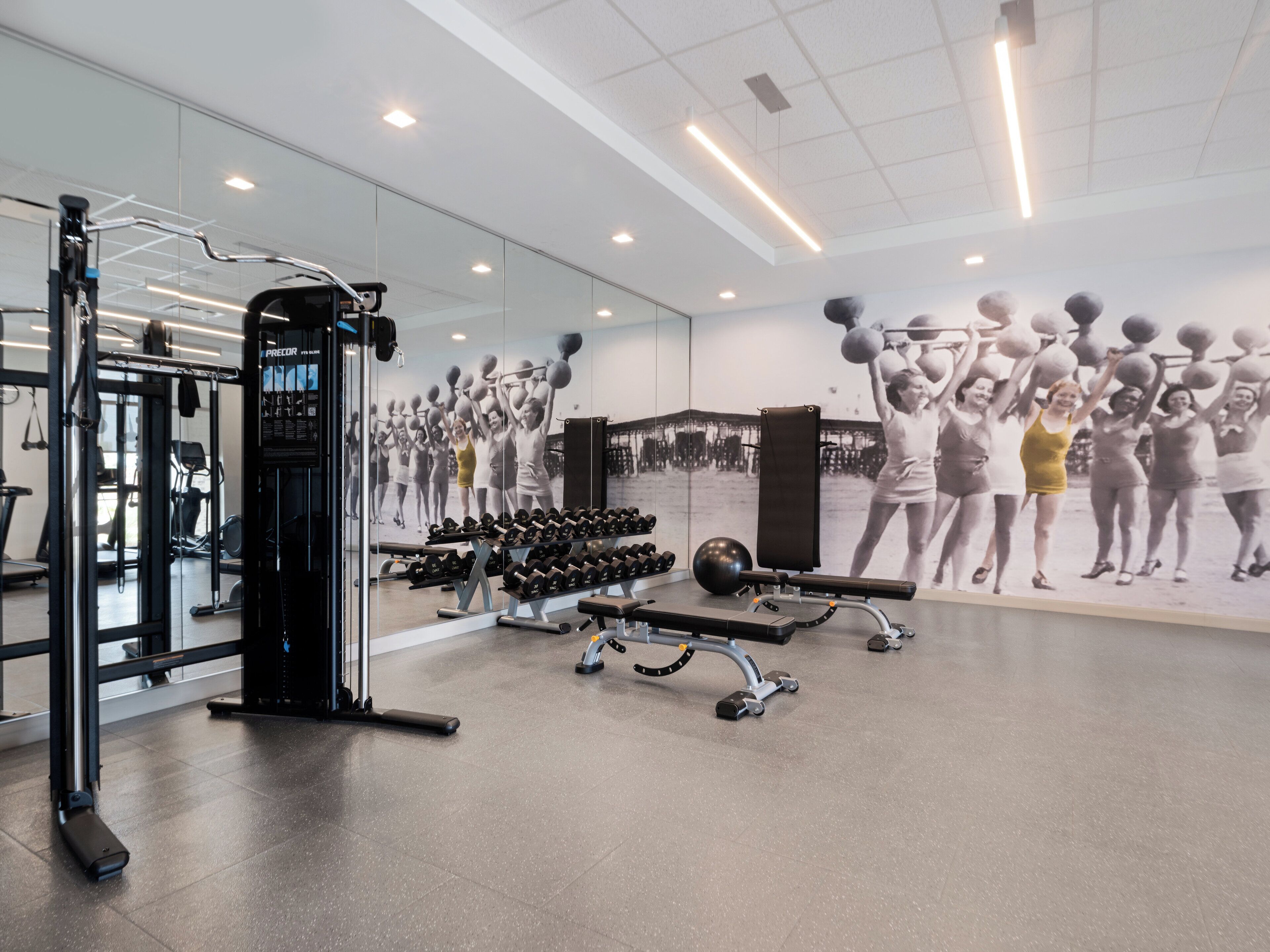 Une salle de sport équipée de matériel d’exercice, dotée d’un murmiroir et ornée d’une grande fresque murale à caractère motivant.