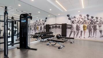 Une salle de sport équipée de matériel d’exercice, dotée d’un murmiroir et ornée d’une grande fresque murale à caractère motivant.