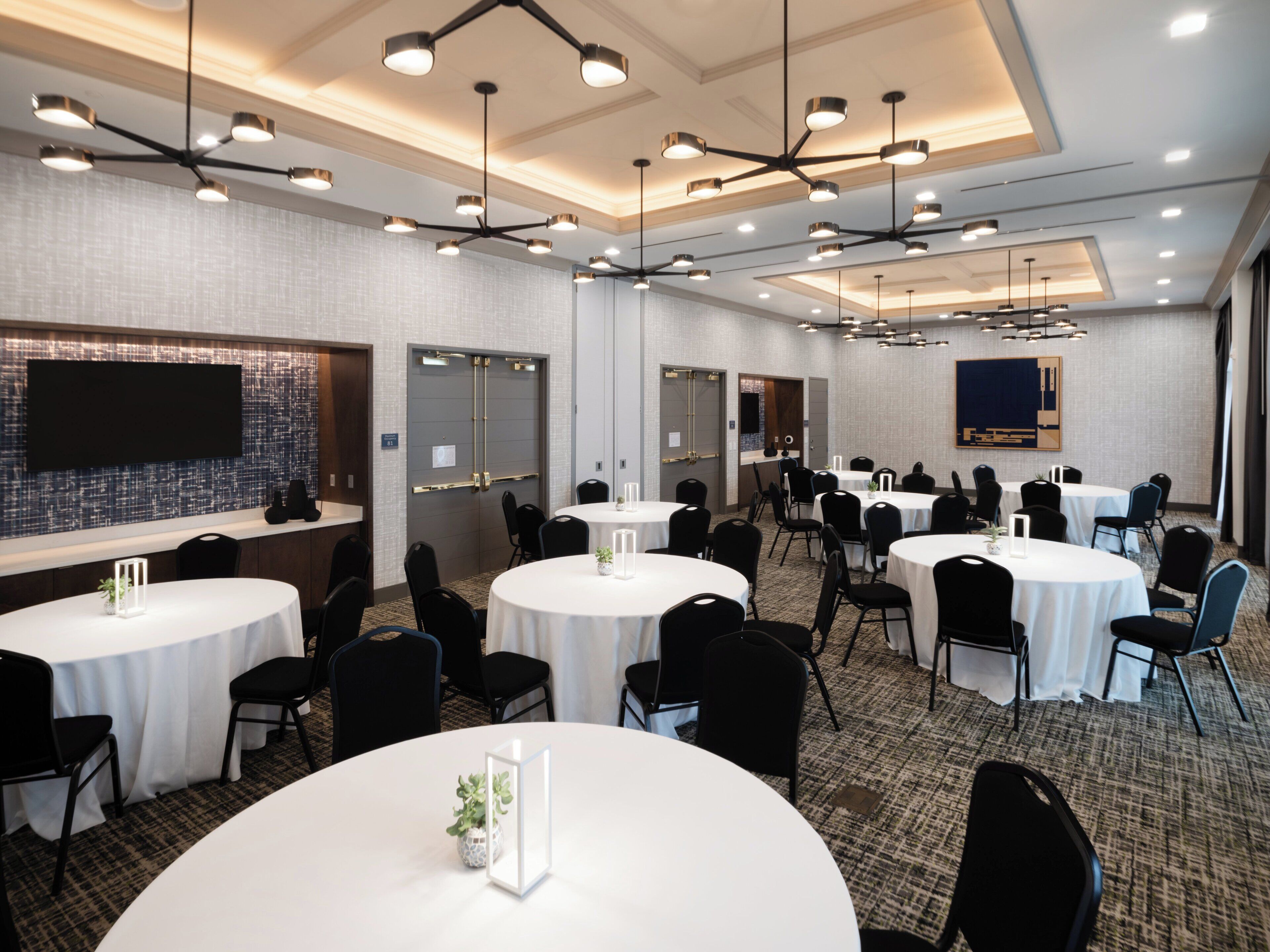 A conference room with multiple round tables, black chairs, and modern lighting fixtures.