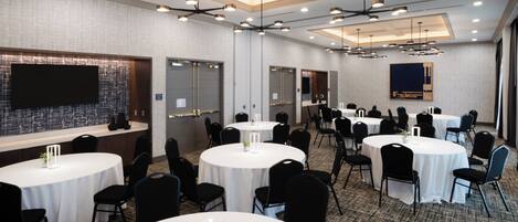 A conference room with multiple round tables, black chairs, and modern lighting fixtures.