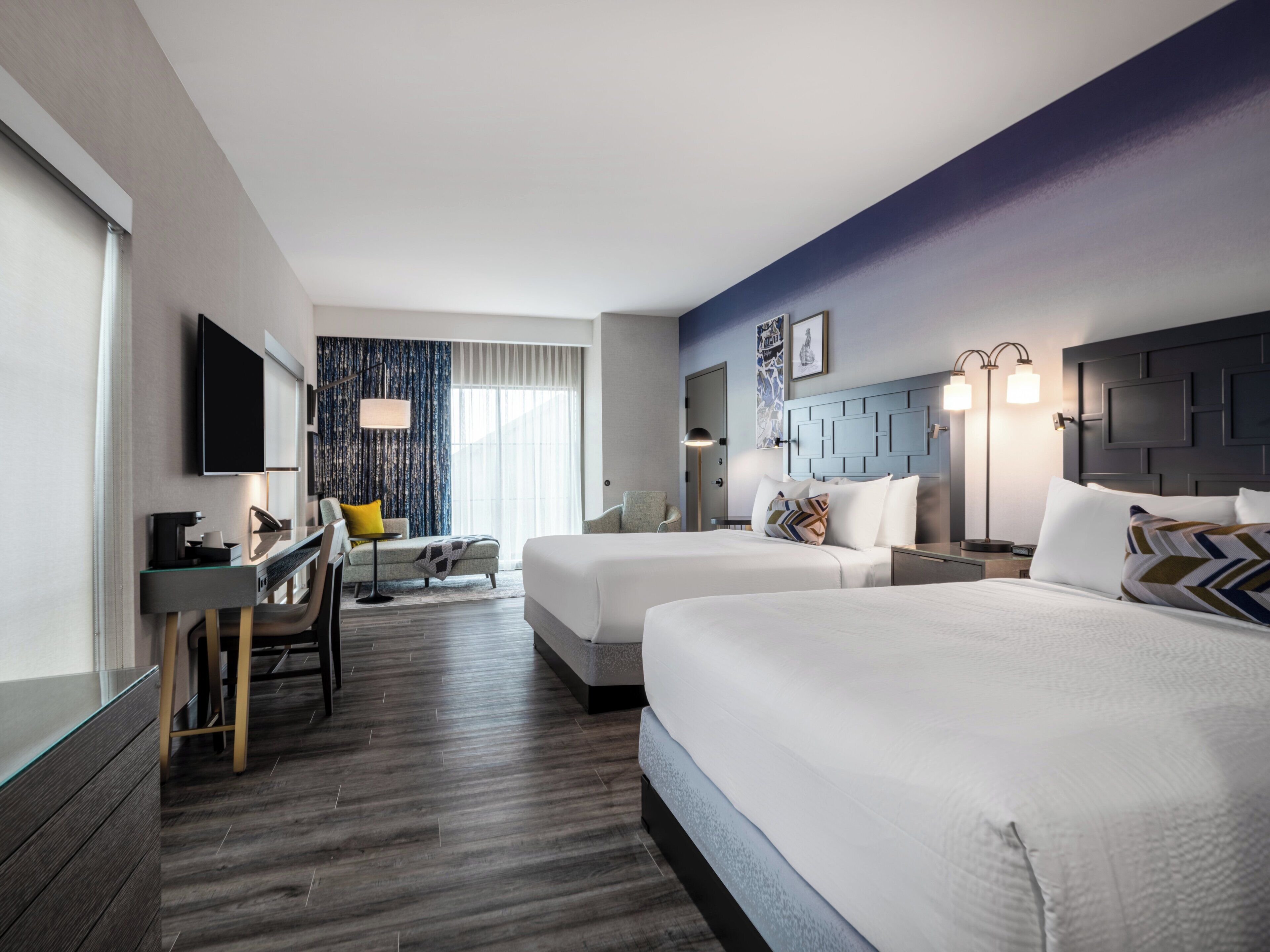 A hotel room with two beds, a desk, a chair, and a television.