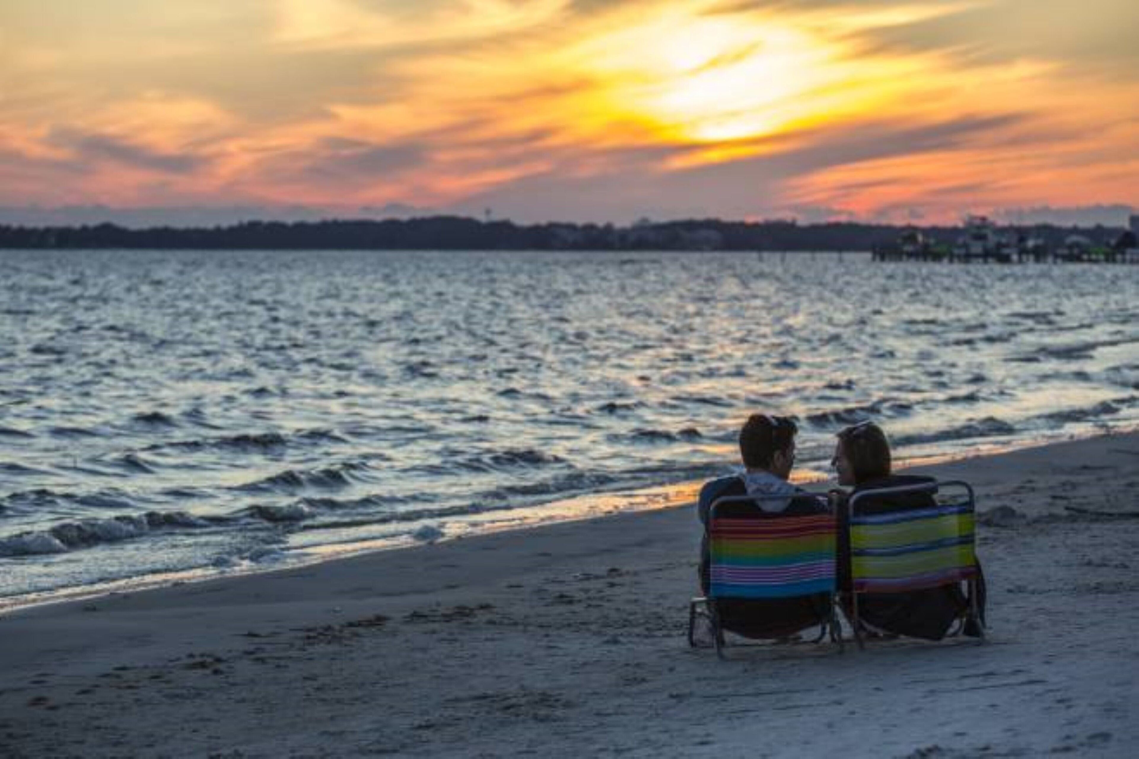 Deux personnes assises sur des chaises de plage, face à l’océan, au moment du coucher du soleil.