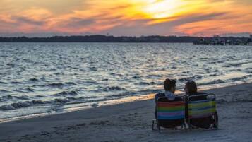 Deux personnes assises sur des chaises de plage, face à l’océan, au moment du coucher du soleil.