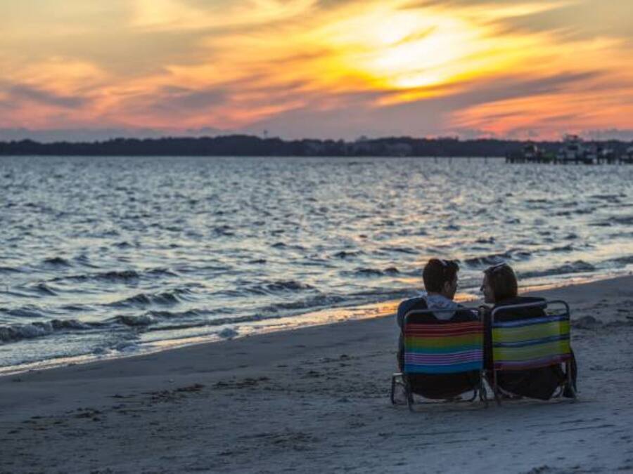Two people sitting on beach chairs facing the ocean during sunset.
