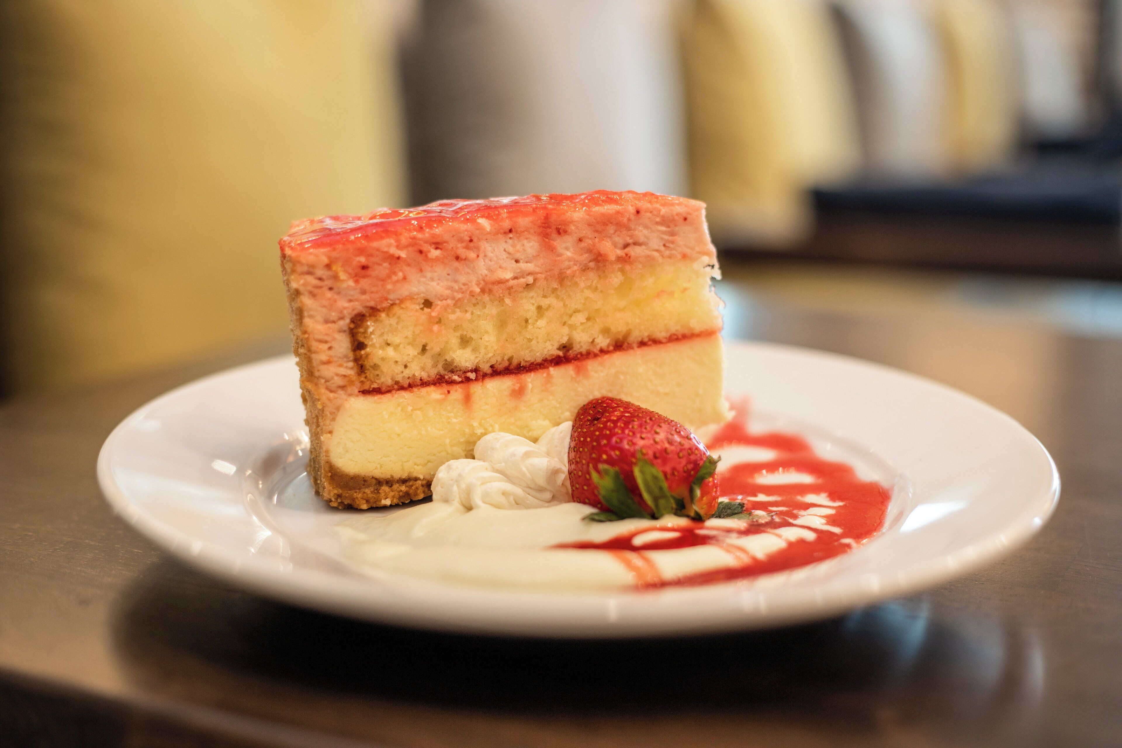 Una porción de pastel de queso con cobertura de fresa y una cucharada de crema batida sobre un plato.