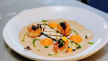 A white plate with a seafood dish, including grilled fish and vegetables, served with a creamy sauce.