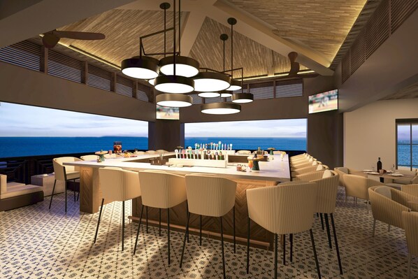 Eine moderne Bar mit einer zentralen Insel, mehreren hängenden Lampen und Blick auf den Ozean.