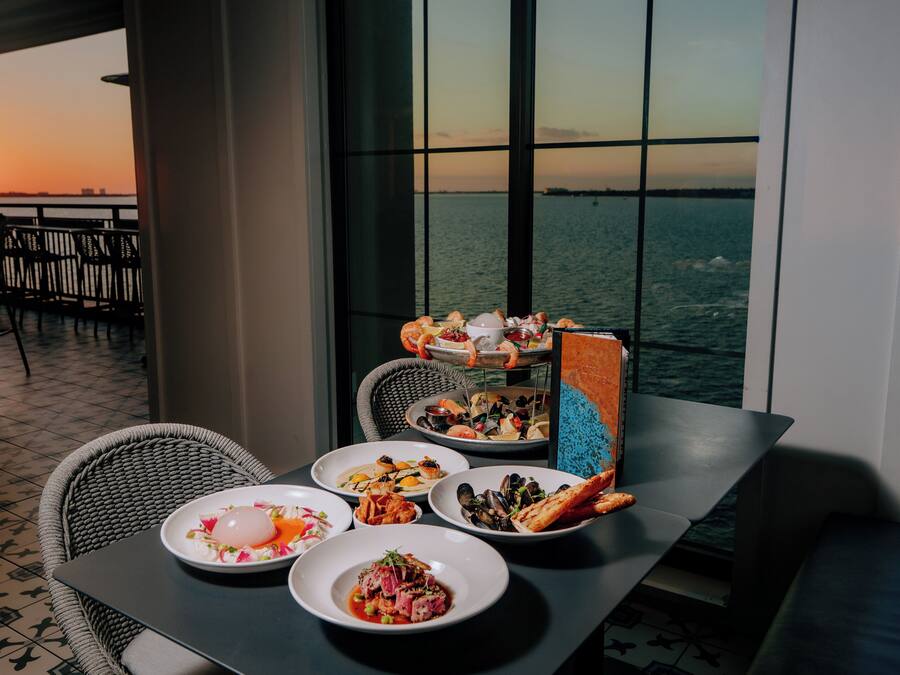 A dining table with various dishes and a view of the ocean at sunset.