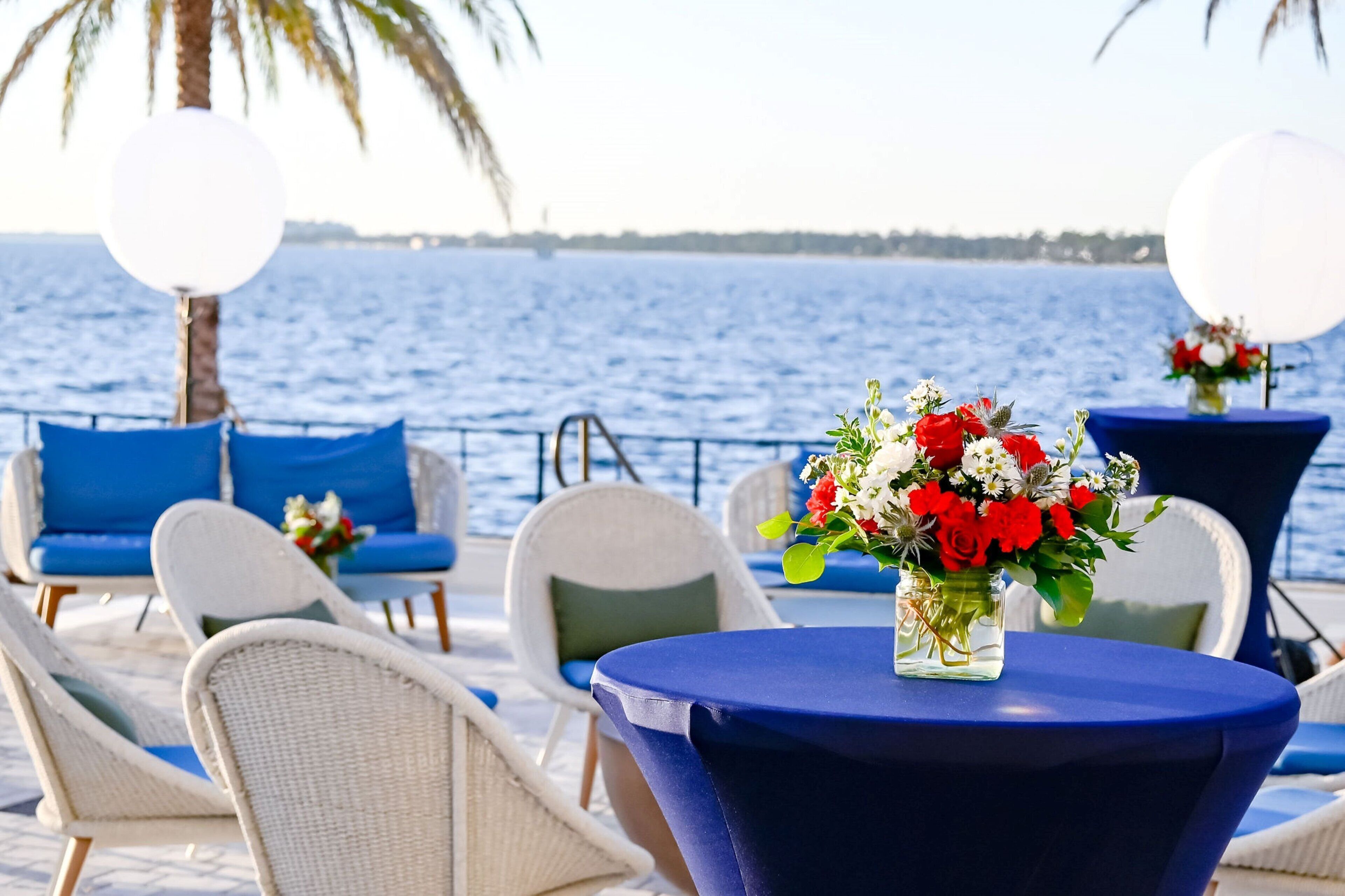 A deck with wicker chairs and a table, a flower vase, and a view of the sea.