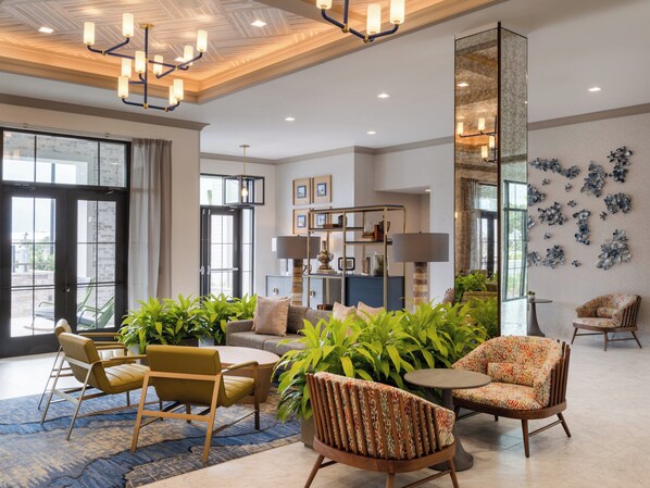 Eine großzügige Lobby mit einem modernen Kronleuchter, einer Sitzecke mit Sofas und Sesseln, einem Couchtisch und einem großen Spiegel.