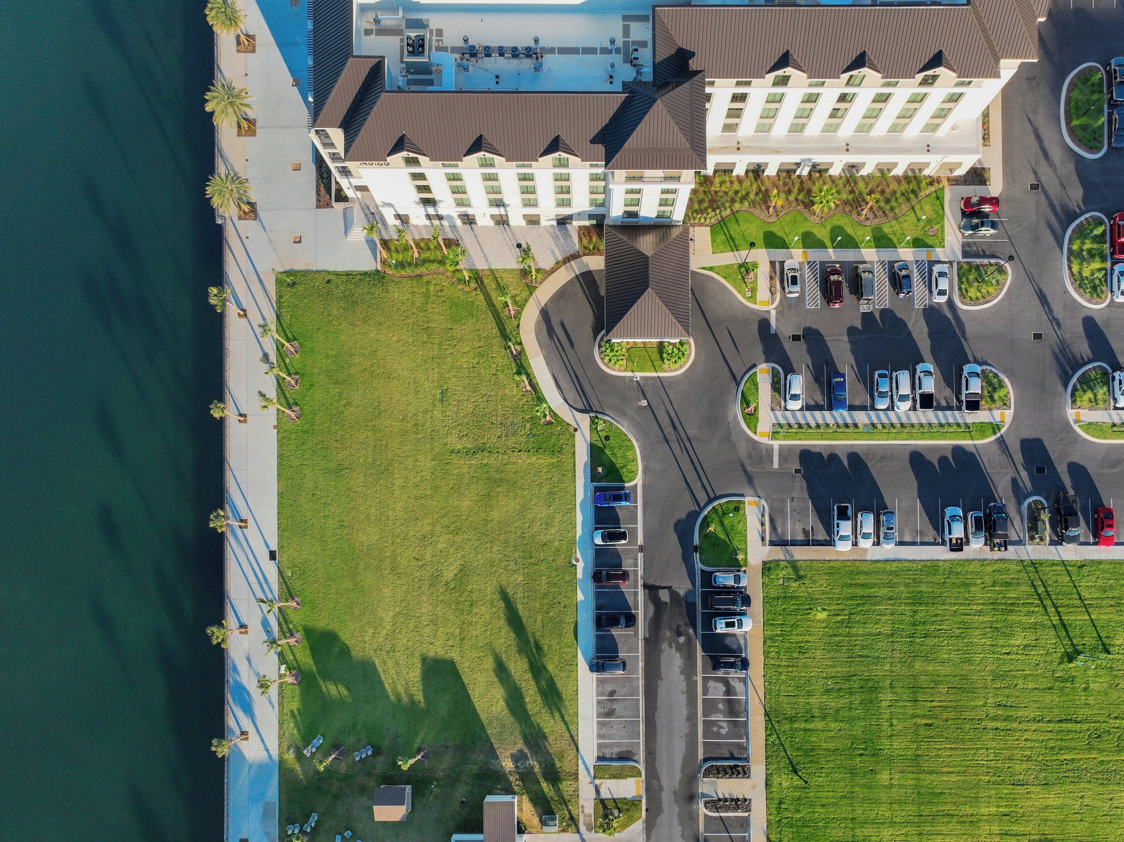 An aerial view of a hotel with a parking lot, a grassy area, and a body of water.