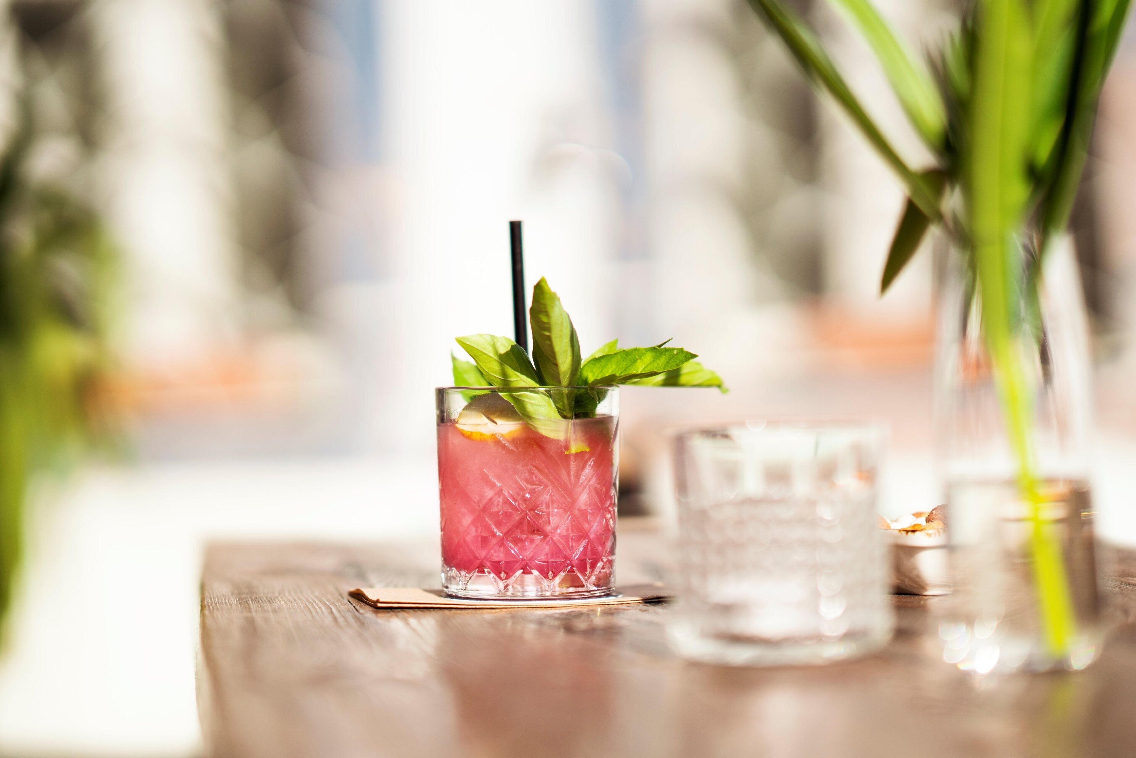 A cocktail glass with a straw and mint leaves on a wooden table.