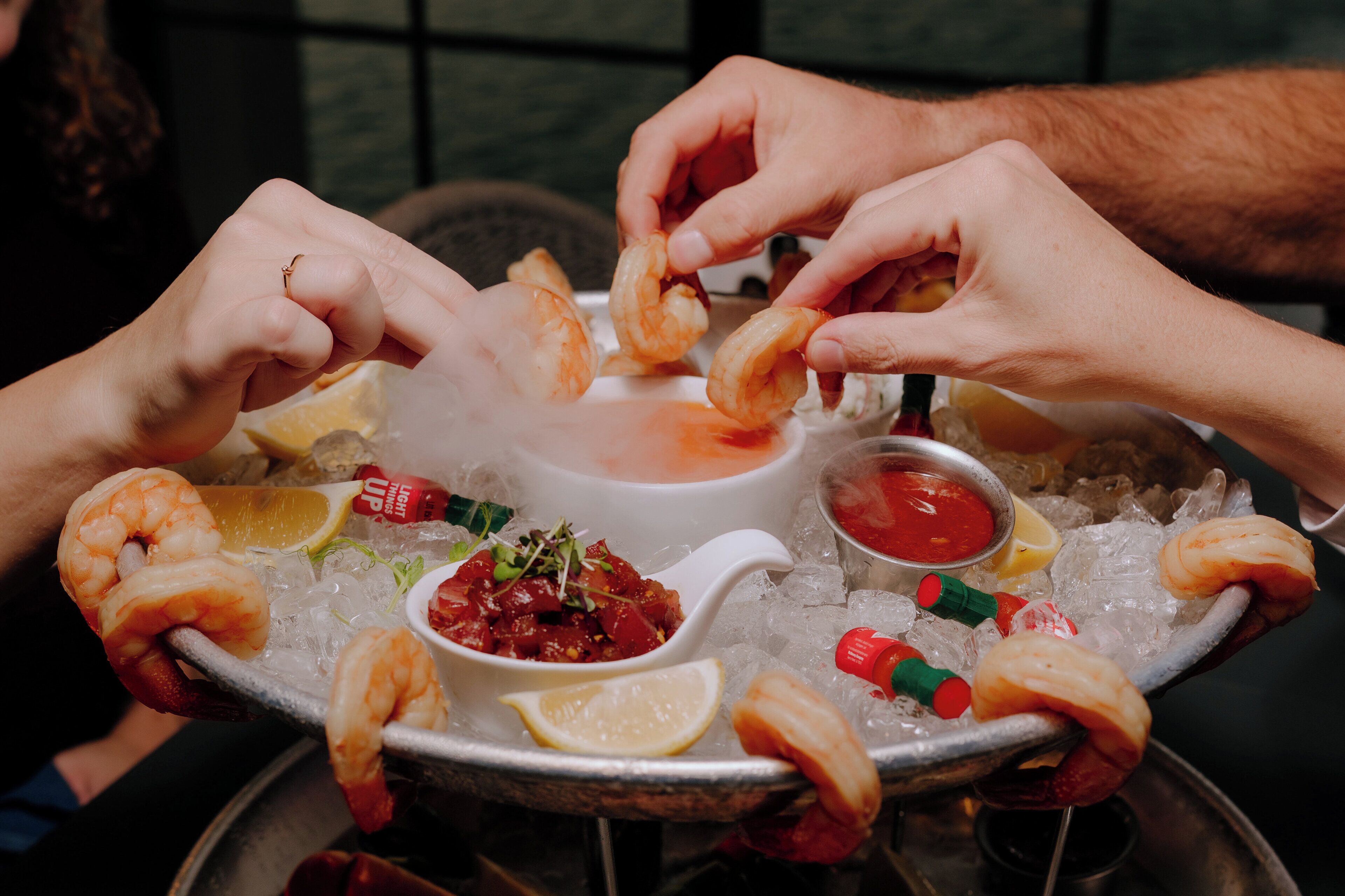 Una bandeja de mariscos con camarones, limón y salsas sobre una base de hielo.