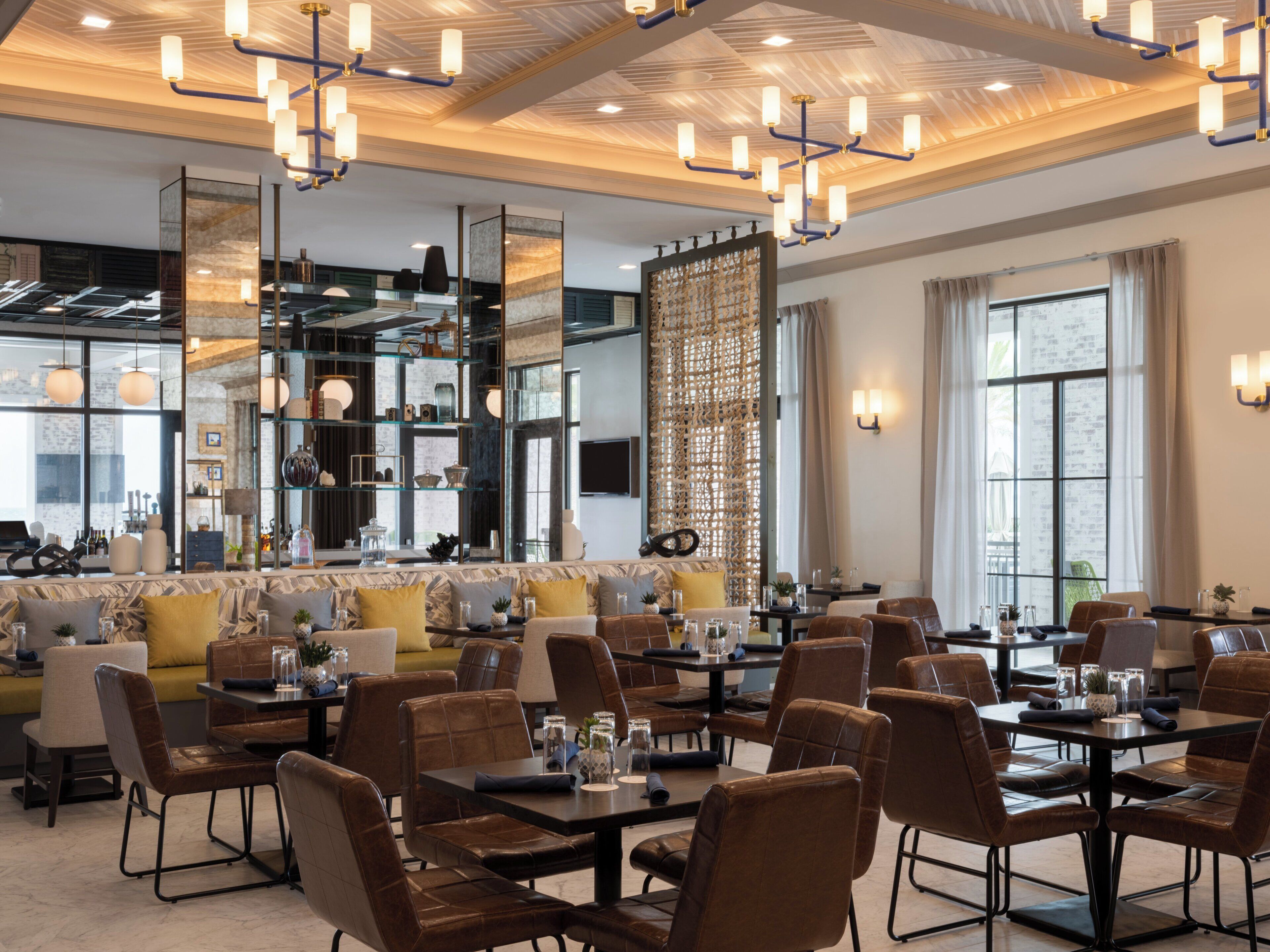 A modern dining area with high ceilings, chandeliers, and a mix of seating including tables and sofas.