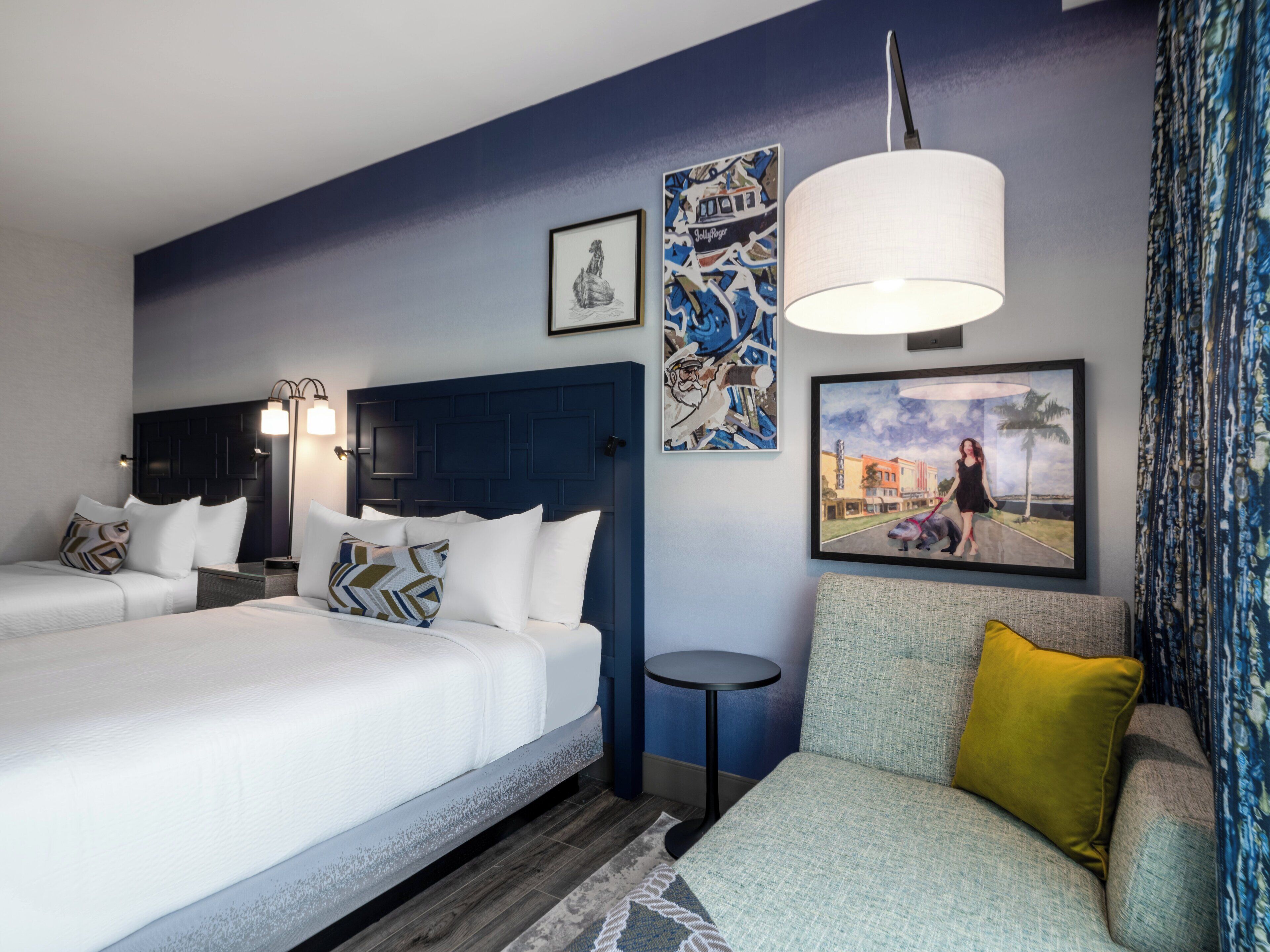 Una habitación de hotel con dos camas, un sofá, una mesita redonda y obras de arte en las paredes.