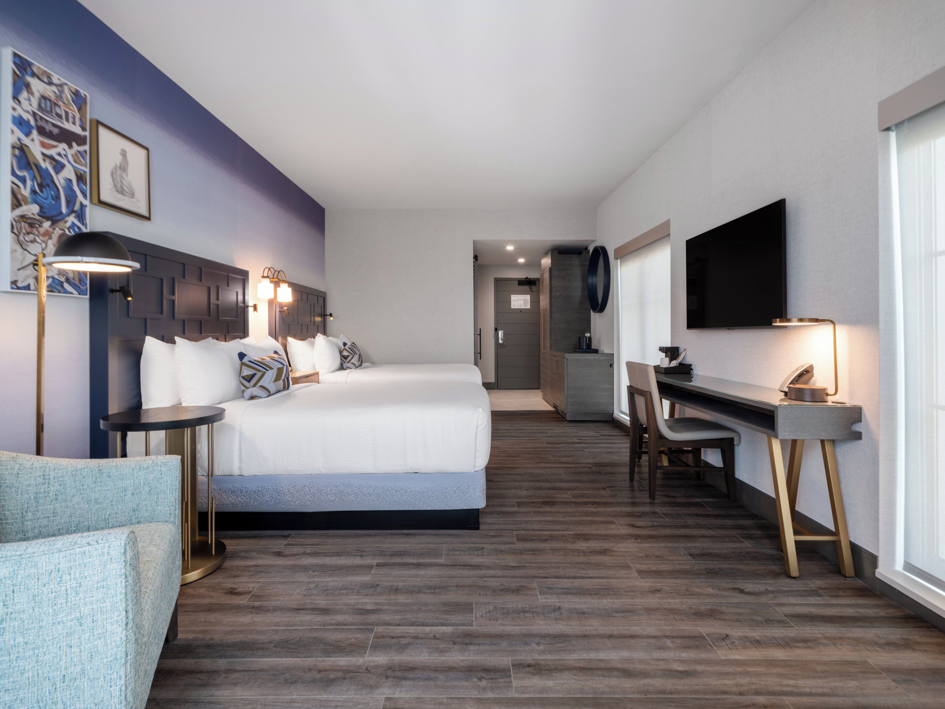 A modern hotel room with a large bed, a desk with a chair, a flat-screen TV, and artwork on the walls.