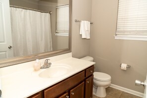 A bathroom with a white sink, a mirror, a toilet, and a shower curtain. - Beautiful home away from home (Raleigh)