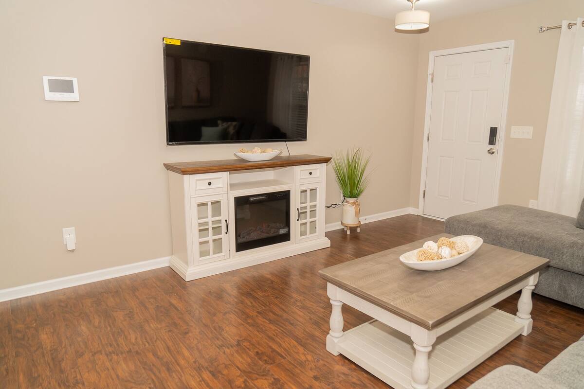 A living room with a flat-screen TV, a fireplace, a coffee table, and a grey sofa.