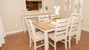 A dining area with a wooden table, white chairs, a mirror, and framed artwork on the wall. - Beautiful home away from home  (Raleigh)